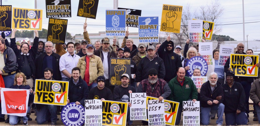 A crowd with signs saying "Millwrights Local 1554 support UAWVW workers," "IUPAT Local 226 supports UAWVW workers," "Solidarity," "Union Yes," "Ver.di," "UAW"