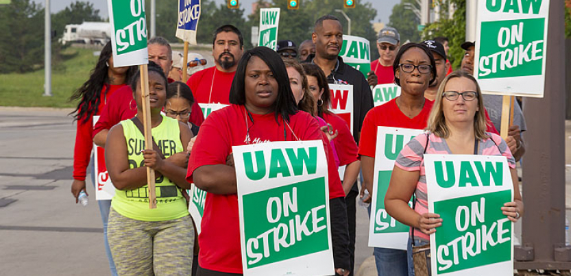 GM strikers march with "UAW on strike" signs. Black and white women in foreground.