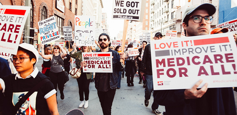 Protest in 2017 with signs that support Medicare for All, people marching in the street
