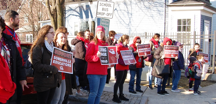 A crowd holding signs saying Support Somerville Educators and Living Wage for Paras