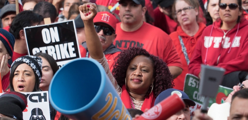 Black woman raising her fist in a crowd of strikers