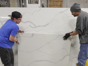 Two workers place a slab of manufactured stone against a larger slab.