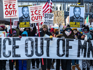 A big crowd carries a banner “ICE out of MN!”