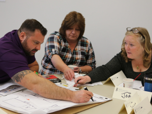 Three workers seated around a table collaborate to draw a hazard map