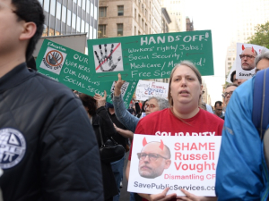 Several workers with signs march towards the camera.  Some say “Hands Off” our workers, our union, Social Security and other items