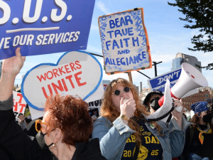A close crowd with signs, including ‘Save our Services’ and someone with a bullhorn