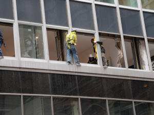 Workers in harnesses work outside windows doing construction.
