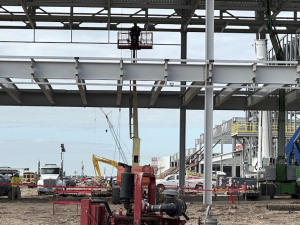 The skeleton of a giant building with a worker in a manlift is shown.