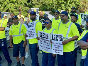 A group of Black men in hi viz green shirts hold signs saying “City workers demand family supporting wages”