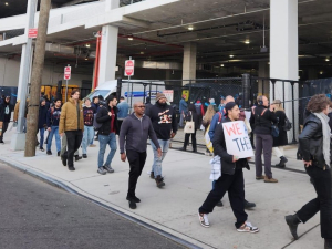 About 25 people walk along a sidewalk, some carrying signs.