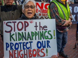A woman holds a sign at a rally that reads Stop the Kidnappings! Protect Our Neighbors!
