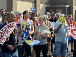 A crowd with UAW signs gathers outside a union hall for a rally.