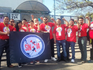 Members of SINTTIA's salary revision committee pose in red union shirts with fists raised up in the air in front of the Federal Center for Conciliation and Labor Registration.