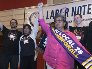 Several people stand on stage with fists raised and with a Labor Notes banner behind them.