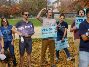 A group of excited people hold blue signs saying “Yes on 1”