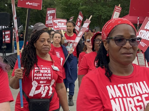 A group of nurses in red T-shirts with signs walk towards the camera.