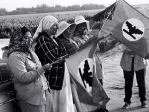 Seven women stand by a car holding a Farmworkers Union flag