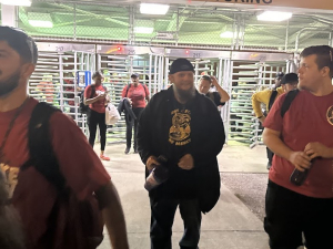 A group of smiling workers leave through factory turnstiles, walking towards the camera.