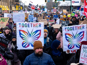 Mass march with many handmade anti-ICE signs. Most prominent are rainbow butterflies with the word "Together." Another in lower right says "How do have money for ICE but not teachers, veterans, childcare, health care, mental heath services, clean water, SNAP?" A flag farther back in crowd shows Star Wars rebellion logo.