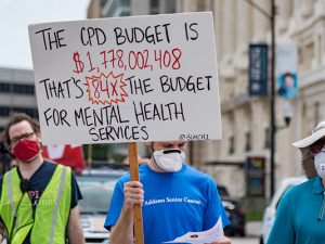 Three people marching against police brutality and for health care in Chicago with a sign