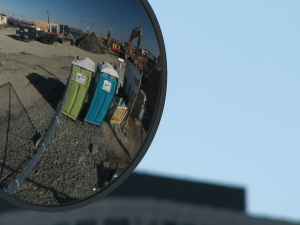Two portajohns are reflected in a truck side mirror.