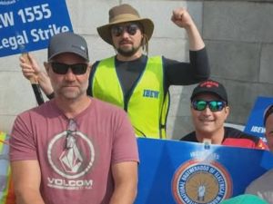 Five men in hats, sunglasses and hi-viz vests hold signs--including one that says IBEW 1555 On Legal Strike
