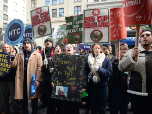 A tight-packed group stands with signs and giant Starbucks cups.