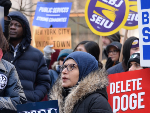 A group of worried-looking protesters hold signs about government cuts