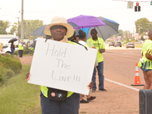 A woman holds a sign reading Hold the Line while others stand on the picket line.
