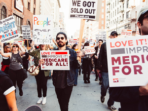 Protest in 2017 with signs that support Medicare for All, people marching in the street