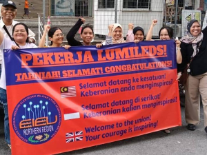 A group of supporters stand behind a red and blue banner congratulating the Lumileds workers on voting for the union and saluting their courage.