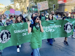 Workers in green aprons march behind a union banner.