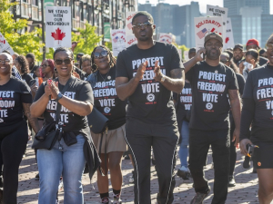 A group of autoworkers with black “Protect Our Freedom to Vote” shirts march