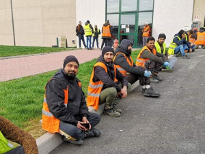 Workers in Italy sitting outside a warehouse on strike in orange vests.