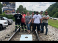 Five people stand on railroad tracks, with a cornhole game at their feet. Some wear "pay us what we are owed" shirts.