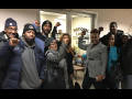 Nine Black film industry parking attendants in coats, smiling with fists up, indoors, in front of an NLRB office in New York City.