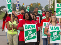 GM strikers march with "UAW on strike" signs. Black and white women in foreground.