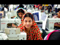 Bangladeshi garment worker at sewing machine looks up, sitting in factory