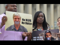 A man and a woman hold signs saying “no NLRB, no voice” with the columns of a government building behind them