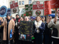 A tight-packed group stands with signs and giant Starbucks cups.