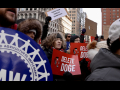A crowd of people hold red and white signs saying “Delete Doge”