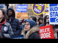 A group of worried-looking protesters hold signs about government cuts