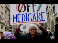 A woman in a big crowd holds up a sign saying ‘hands off Medicare’