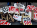 stack of picket signs including "don't raise tuition, fund CUNY contract," "good jobs now, make Wall Street pay," "CUNY invest in New York," "help the people, not the billionaires," and "CUNY needs competitive salaries"