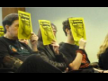 Protesters sitting in a row in a meeting hold up yellow posters with a picture of slain worker Juan Baten.