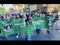 Workers in green aprons march behind a union banner.