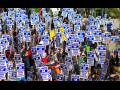 View from above of a sea of marchers outdoors, all carrying matching printed "UAW on strike" picket signs