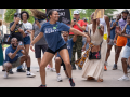 A Black dancer dances joyfully on the picket line, her long hair streaming out behind her. She is wearing a blue AGMA shirt. A delighted crowd, also mostly Black, surrounds her watching and taking photos -- some also wear AGMA shirts. The photo is full of energy, motion, and joy.