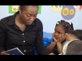 A teacher reads to kindergarteners, one of whom has her chin on her hands and seems to be rapt by the story