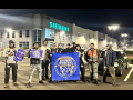 Siemens workers pose in front of the factory in the dark behind a blue banner that says Siemens Workers United.